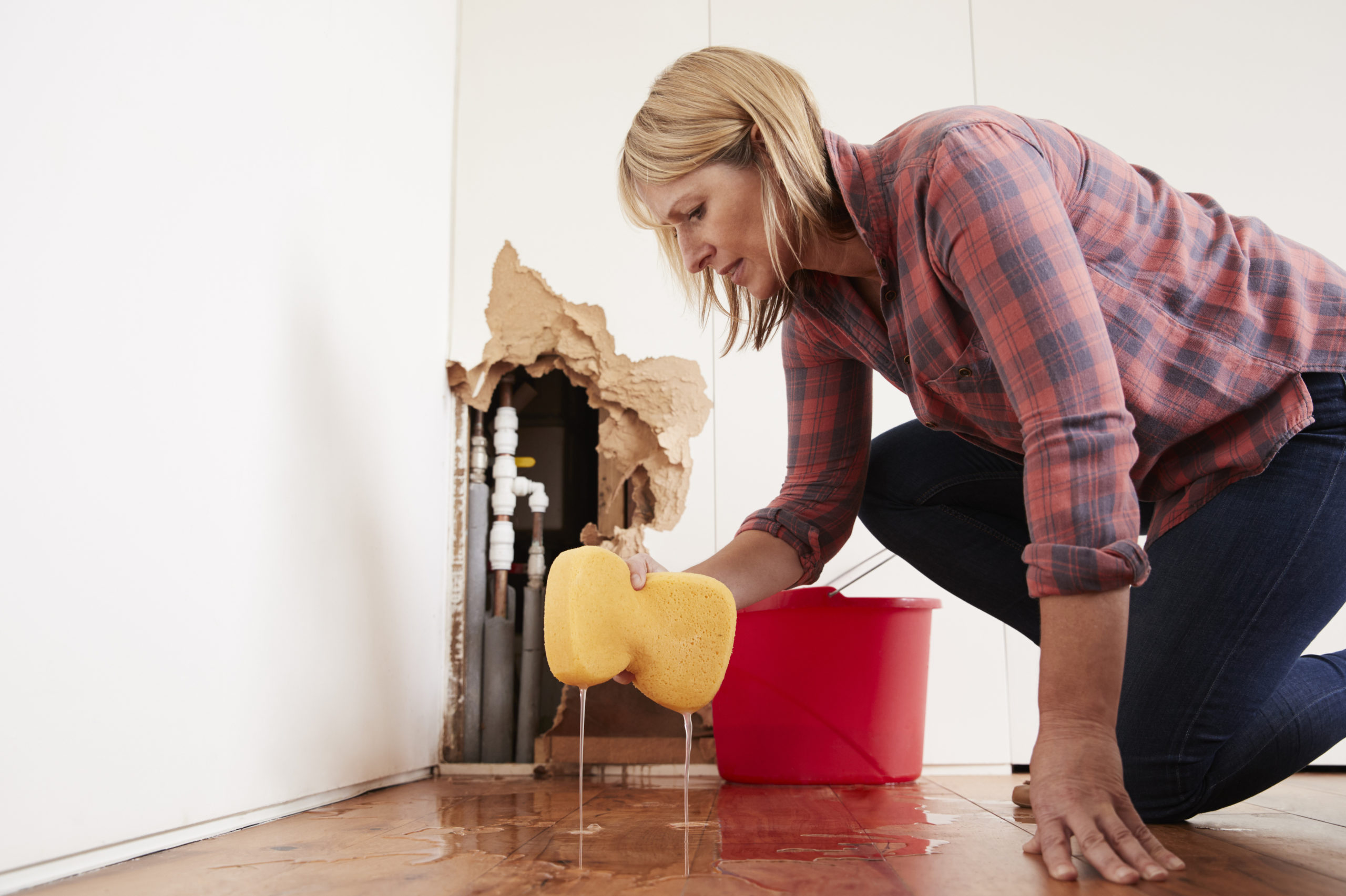 Worried woman mopping up water from a burst pipe.